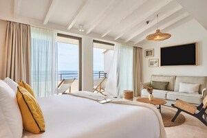 Une chambre d’hôtel avec un grand lit, un canapé, une petite table et un balcon donnant sur la mer.