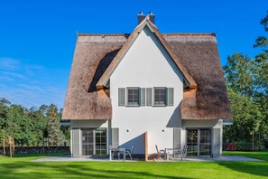 Une maison moderne avec un toit à forte pente, de grandes fenêtres et une pelouse bien entretenue.