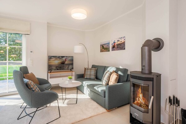 A modern living room with a grey sofa, a small coffee table, a TV, and a wood-burning stove.