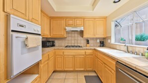 Una cocina con armarios de madera, estufa, refrigerador y ventana con vista a la vegetación.