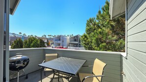Un balcón con mesa y sillas, una parrilla y vistas a edificios y árboles cercanos.