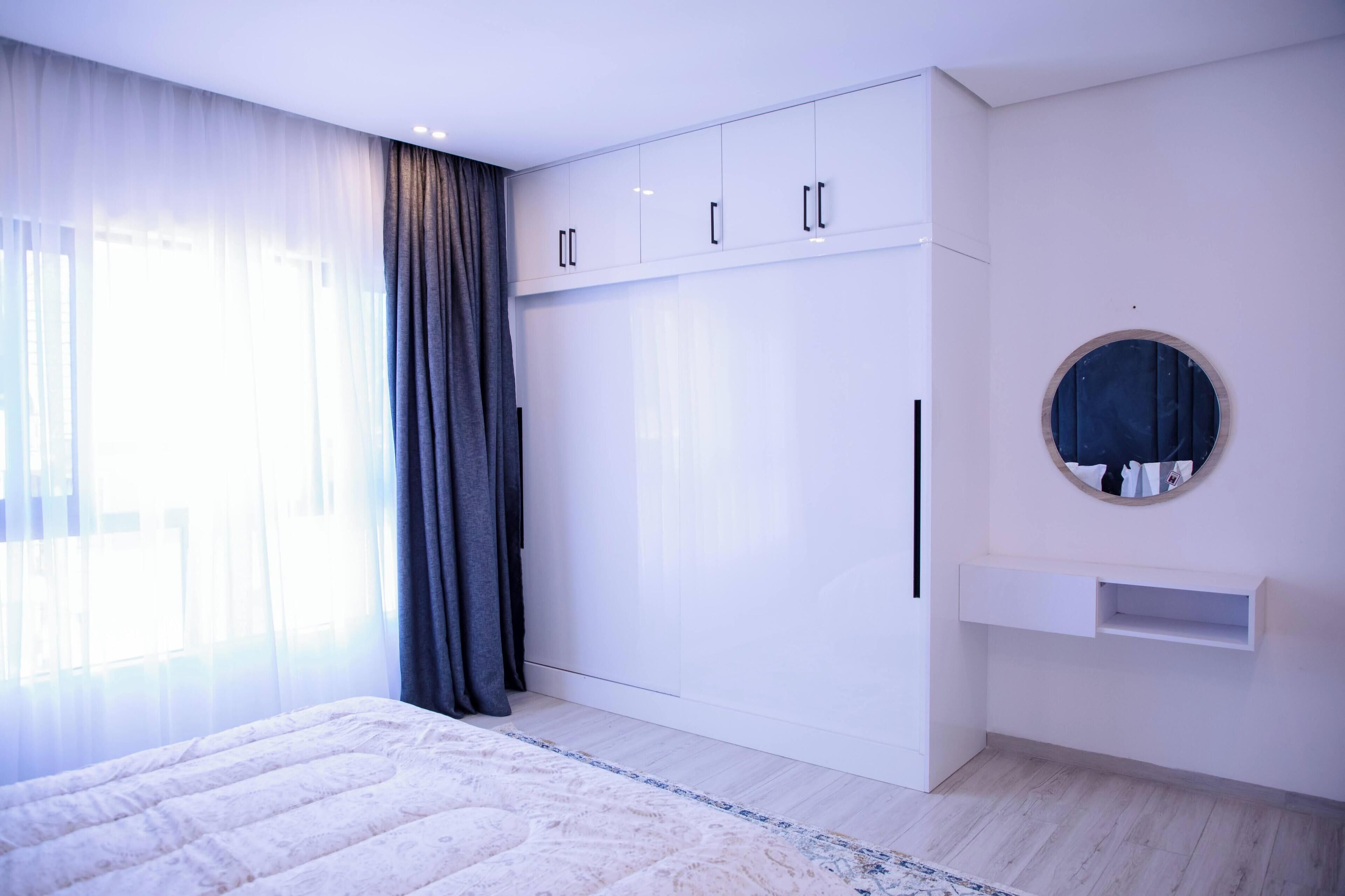A bedroom with a bed, a wardrobe, a mirror, and a window with curtains.