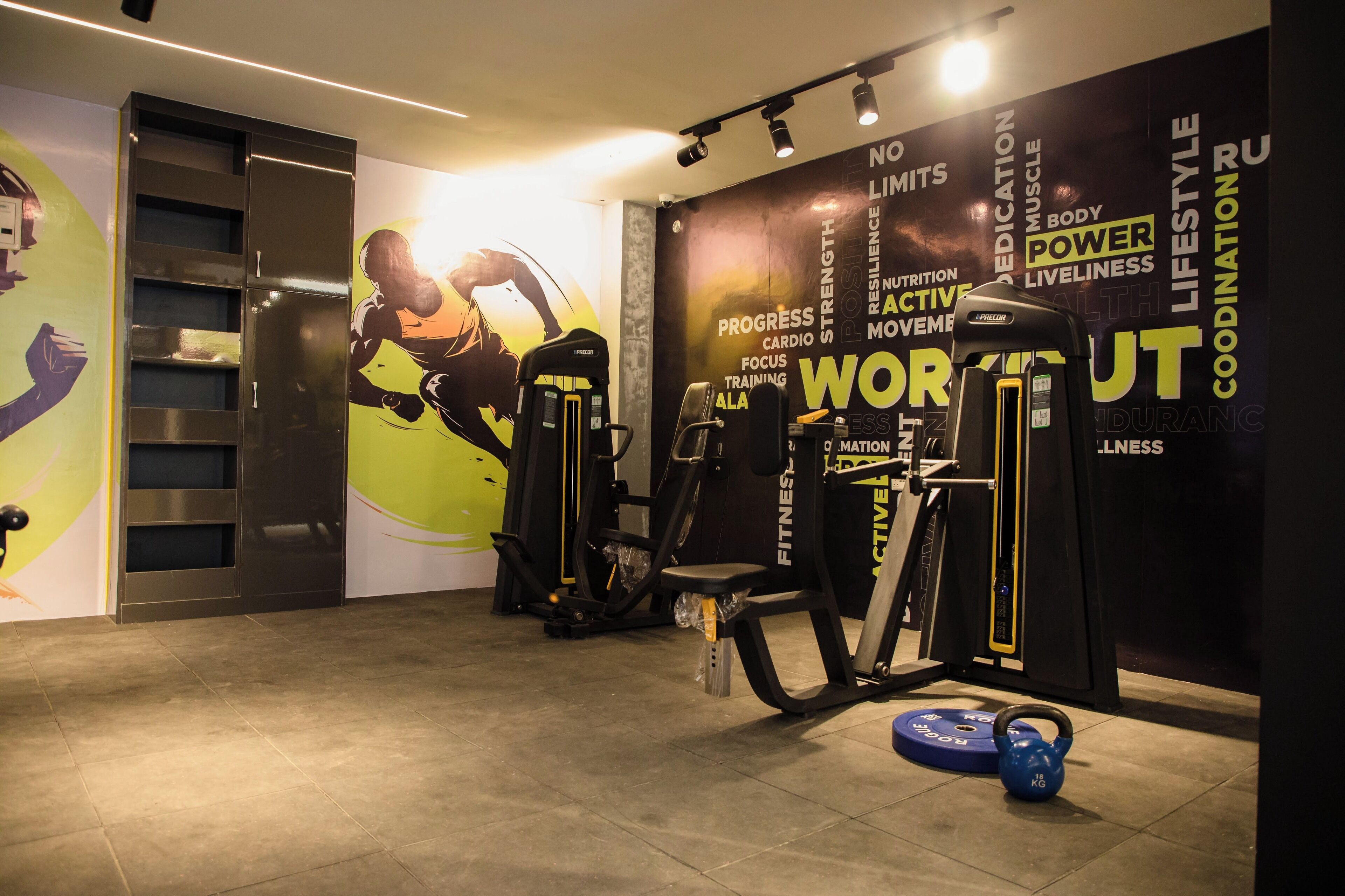 Une salle de sport équipée de matériel d’exercice, un mur orné de citations motivantes et un kettlebell bleu posé sur le sol.