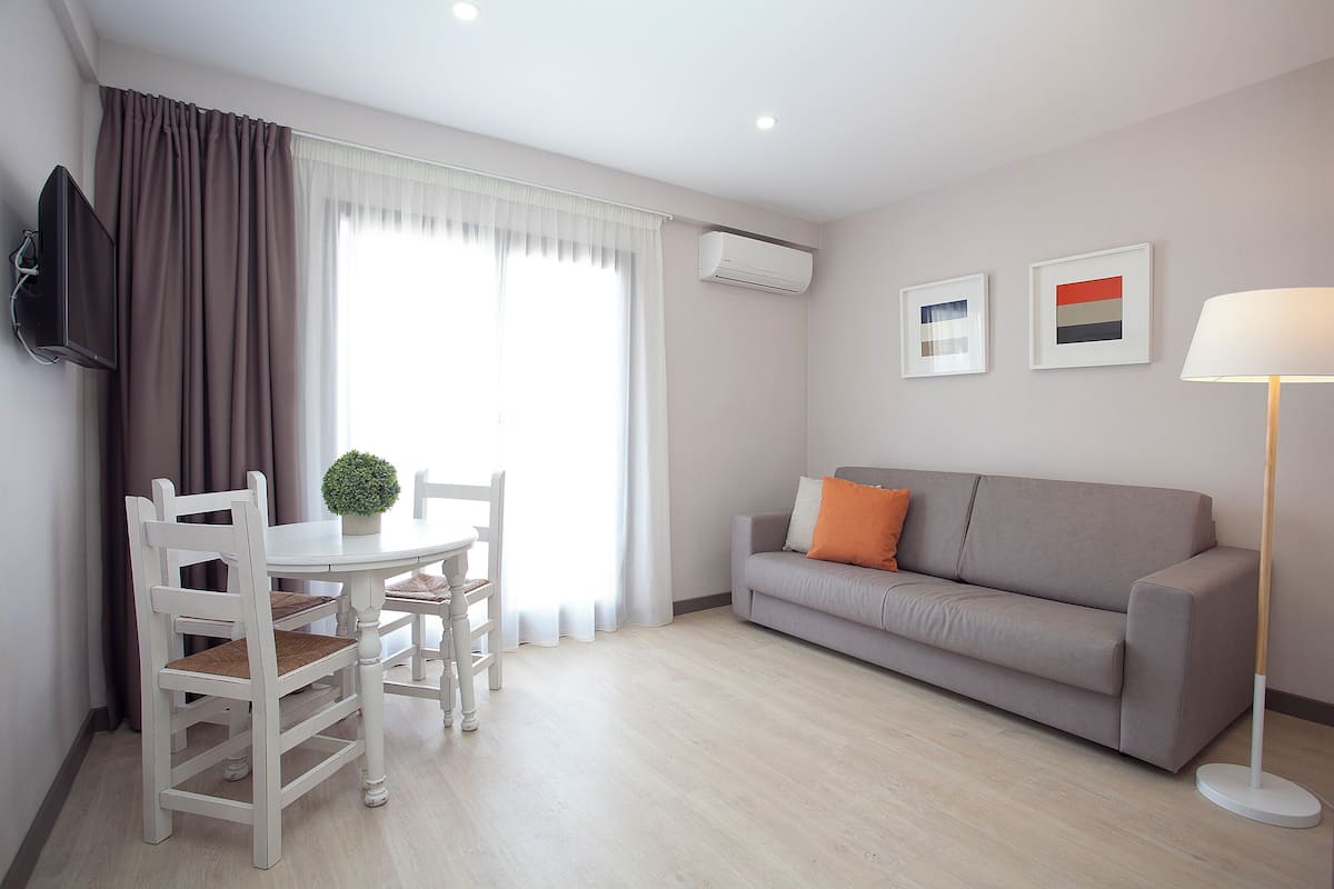 A modern living room with a grey sofa, white dining table, and chairs.