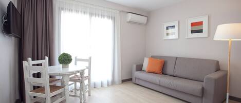 A modern living room with a grey sofa, white dining table, and chairs.