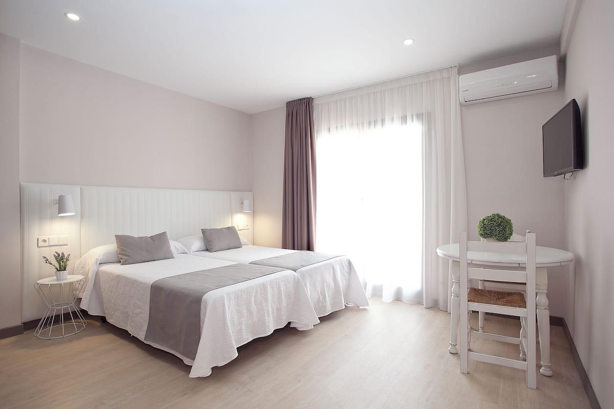 A modern bedroom with a bed, bedside tables, a small round table, and a TV mounted on the wall.