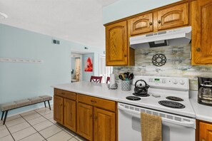 Una cocina con armarios de madera, una encimera blanca, una estufa y un hervidor.