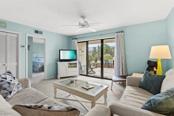 A living room with a television, a coffee table, and a sofa. There is a sliding glass door leading to an outdoor area.