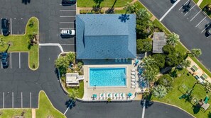 An aerial view of a hotel with a swimming pool, parking lot, and surrounding greenery.