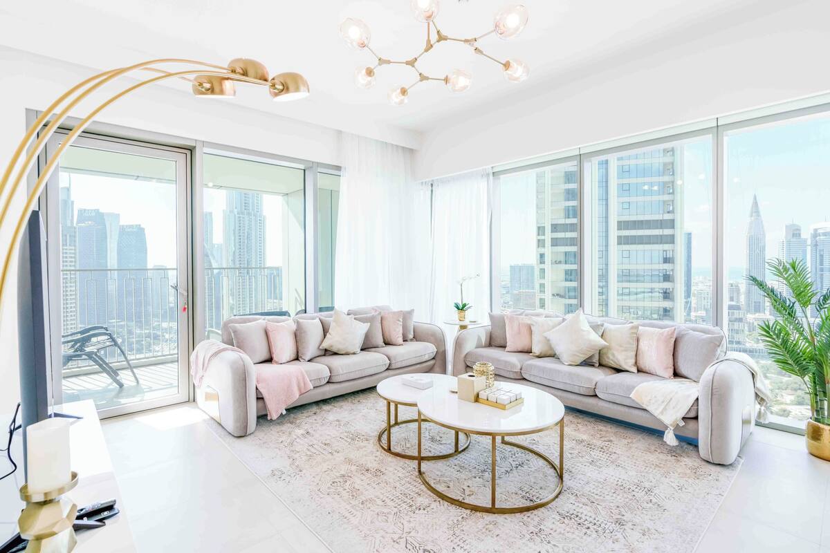 A spacious living room with a large window, a sofa set, a coffee table, and a chandelier.
