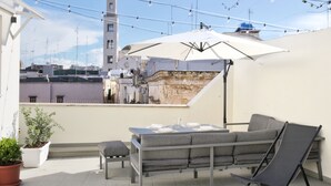 A rooftop terrace with a table and chairs, a potted plant, and a view of a historic building with a tower. - Dimora Riccardi San Nicola (Bari)