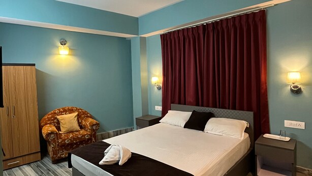A bedroom with a bed, a chair, a wardrobe, and nightstands with lamps. - Arrived Inn (Gyalshing)
