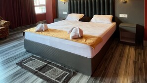 A hotel room with a large bed, two bedside lamps, a wooden floor, and a view of the outside through the window. - Arrived Inn (Gyalshing)