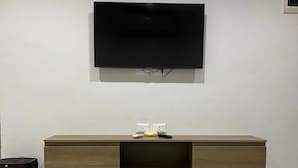 A modern living room with a flat-screen TV mounted on the wall, a wooden entertainment unit below, and a tiled floor.