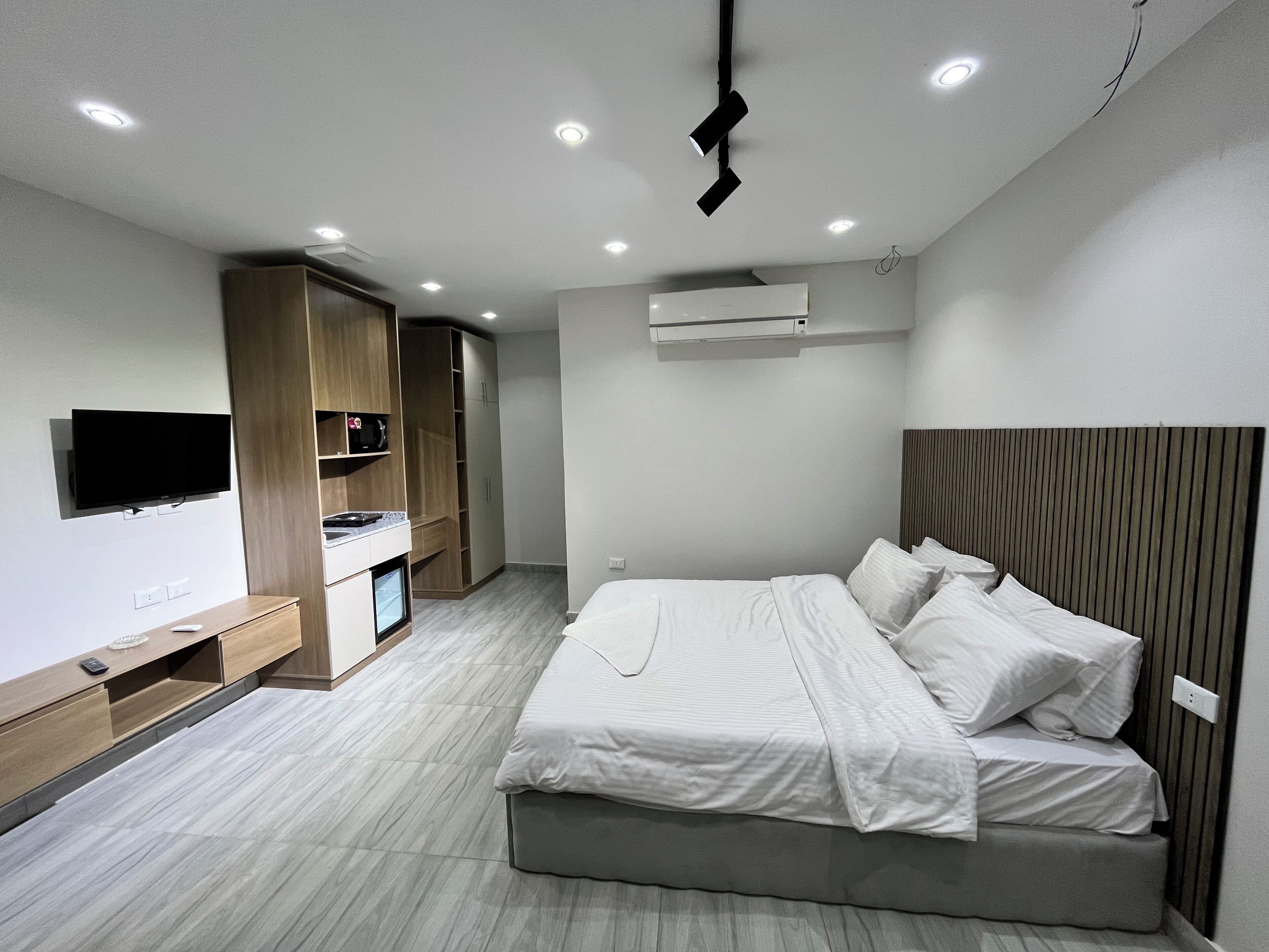 A modern bedroom with a bed, built-in TV, wardrobe, and air conditioning unit.