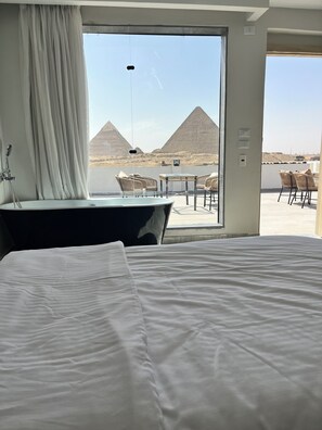 Een hotelkamer met een groot bed, een badkamer met een bad en uitzicht op de piramides.