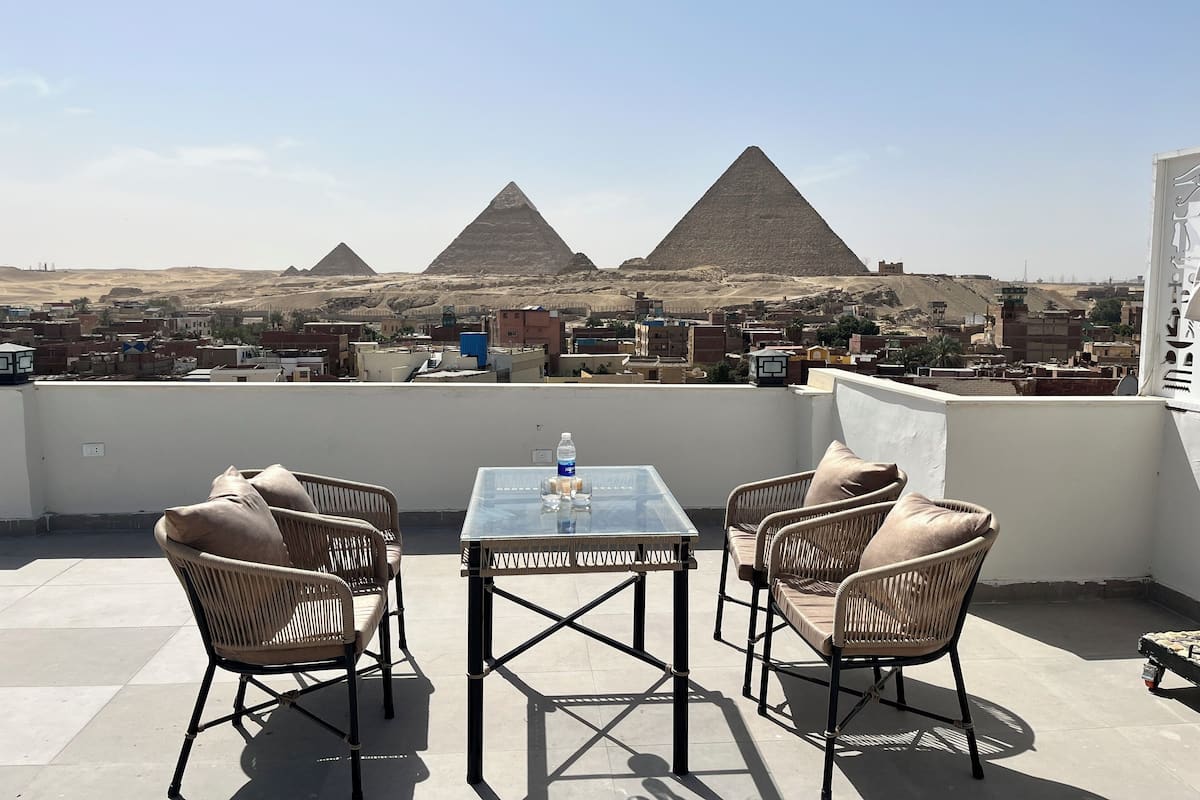 Una terrazza sul tetto con sedie in vimini e un tavolo in vetro, con vista sulle piramidi.