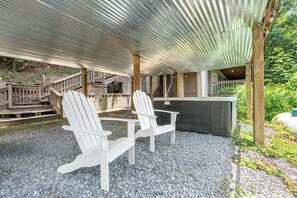 A covered outdoor seating area with Adirondack chairs, a grill, and a wooden deck.