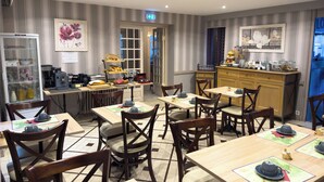 A dining area with multiple tables and chairs, a refrigerator, a coffee machine, and various kitchen items on the counter. - Logis hôtel des voyageurs (Tarnac)