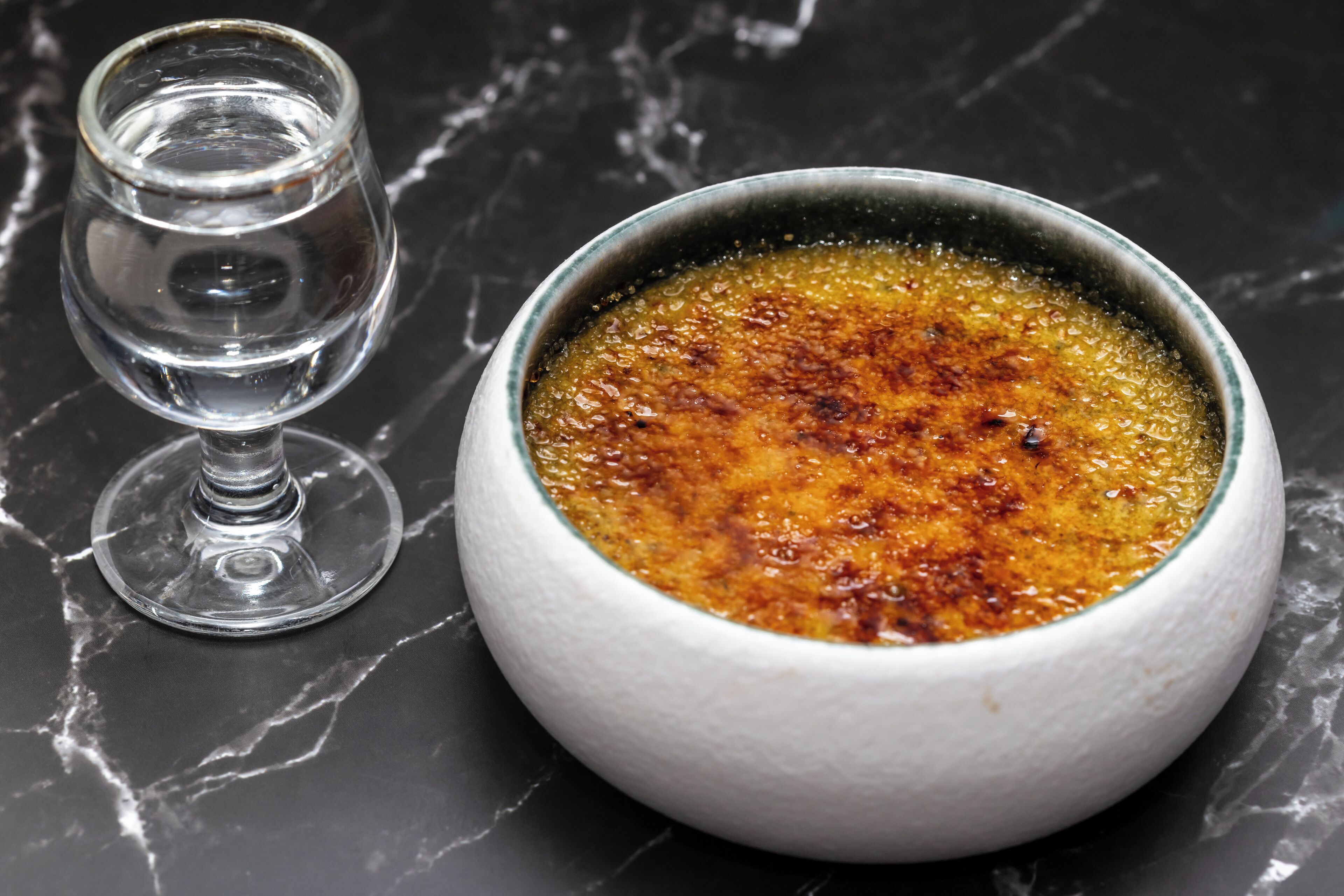 A bowl of crème brûlée on a marble surface.