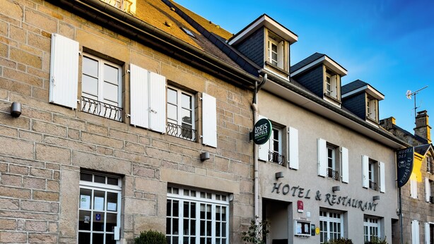 A hotel with a stone facade, multiple windows with shutters, outdoor seating, and a clear blue sky. - Logis hôtel des voyageurs (Tarnac)