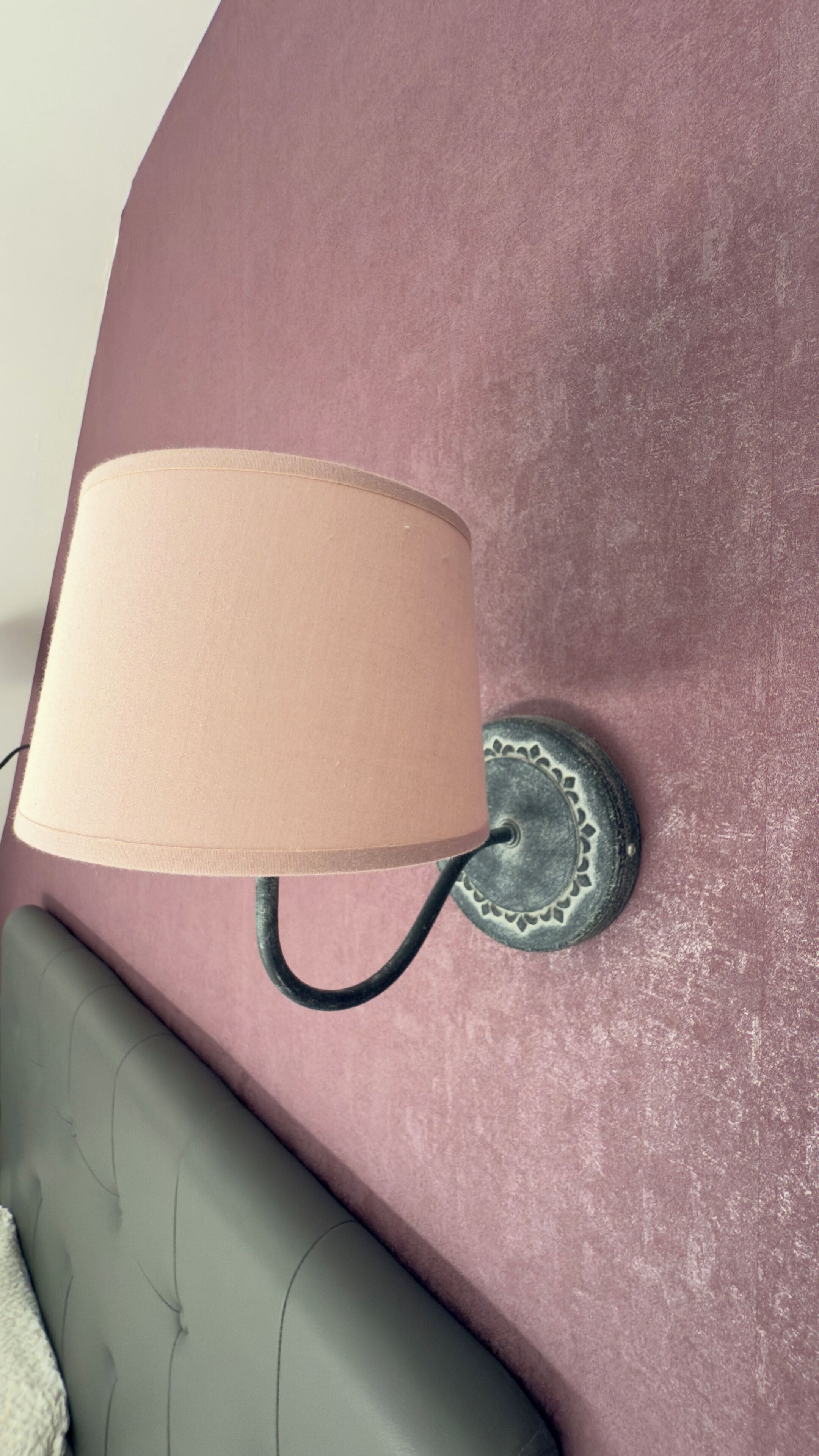 A wall-mounted lamp with a beige shade attached to a textured pink wall.