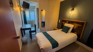 Hotellihuone, jossa on sänky, työpöytä, tuoli, televisio ja puhelin.