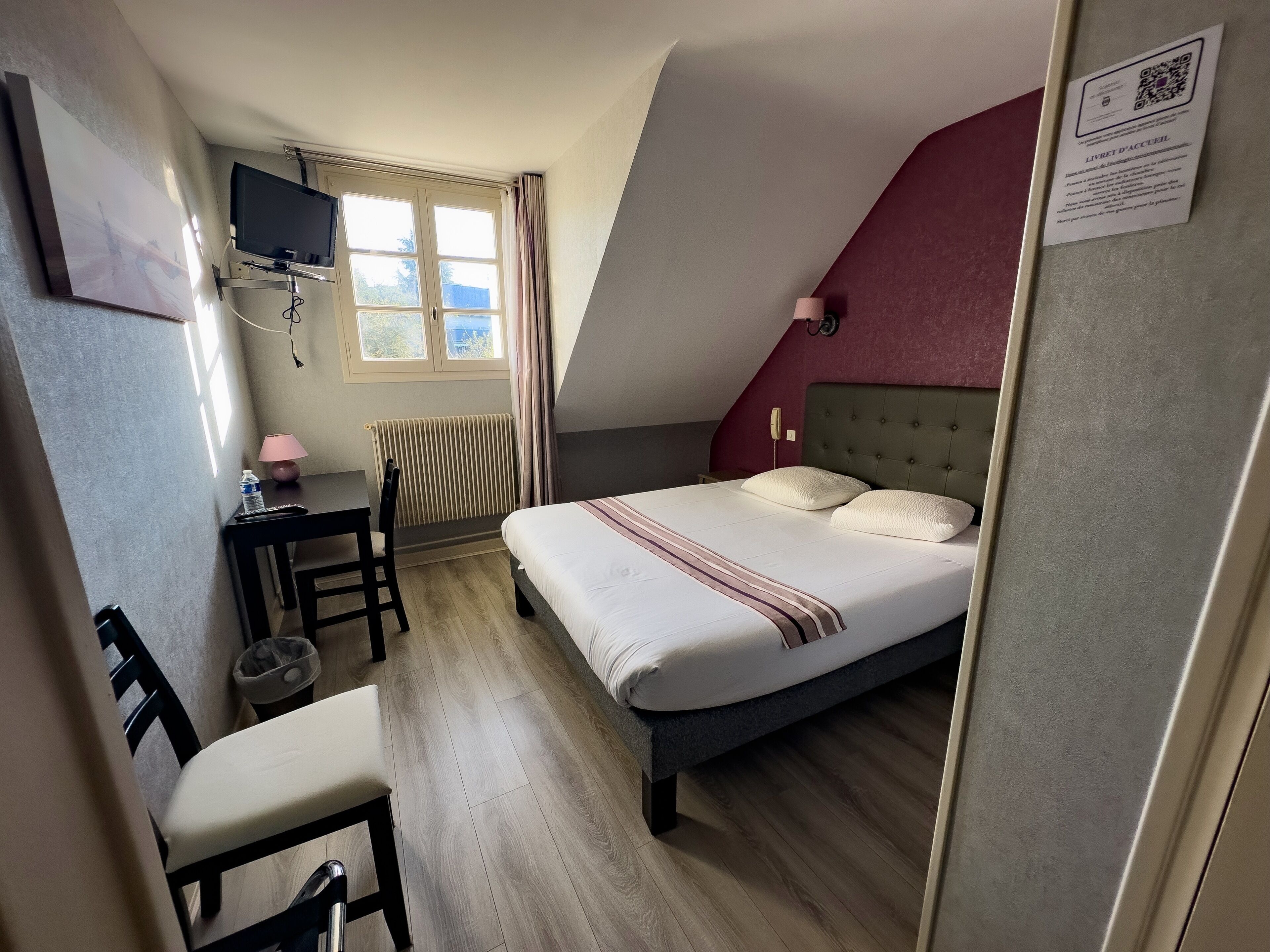 Un dormitorio con una cama, un escritorio, una silla, un televisor y una ventana.