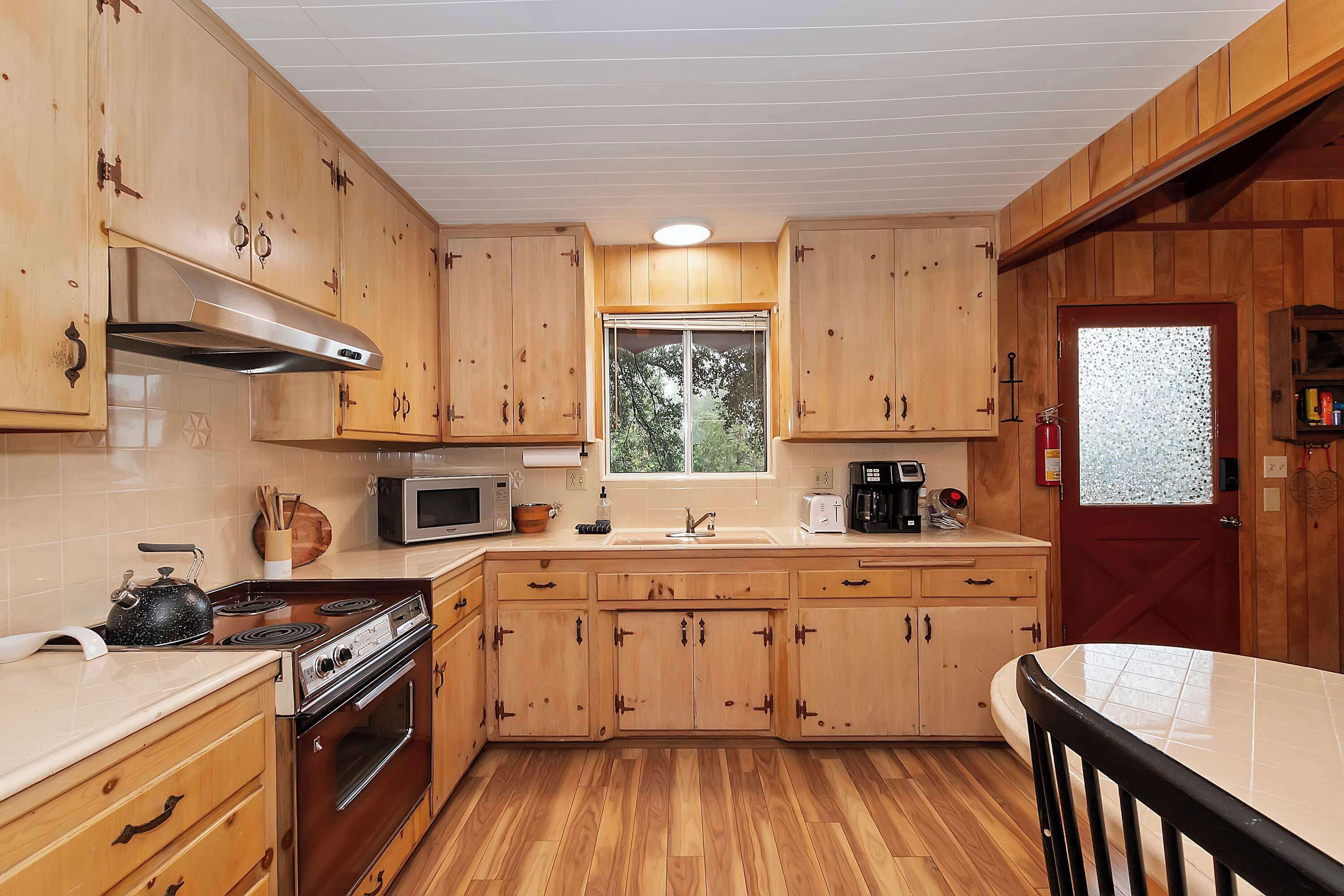 A kitchen with wooden cabinets, a stove, microwave, and a window with a view of trees.