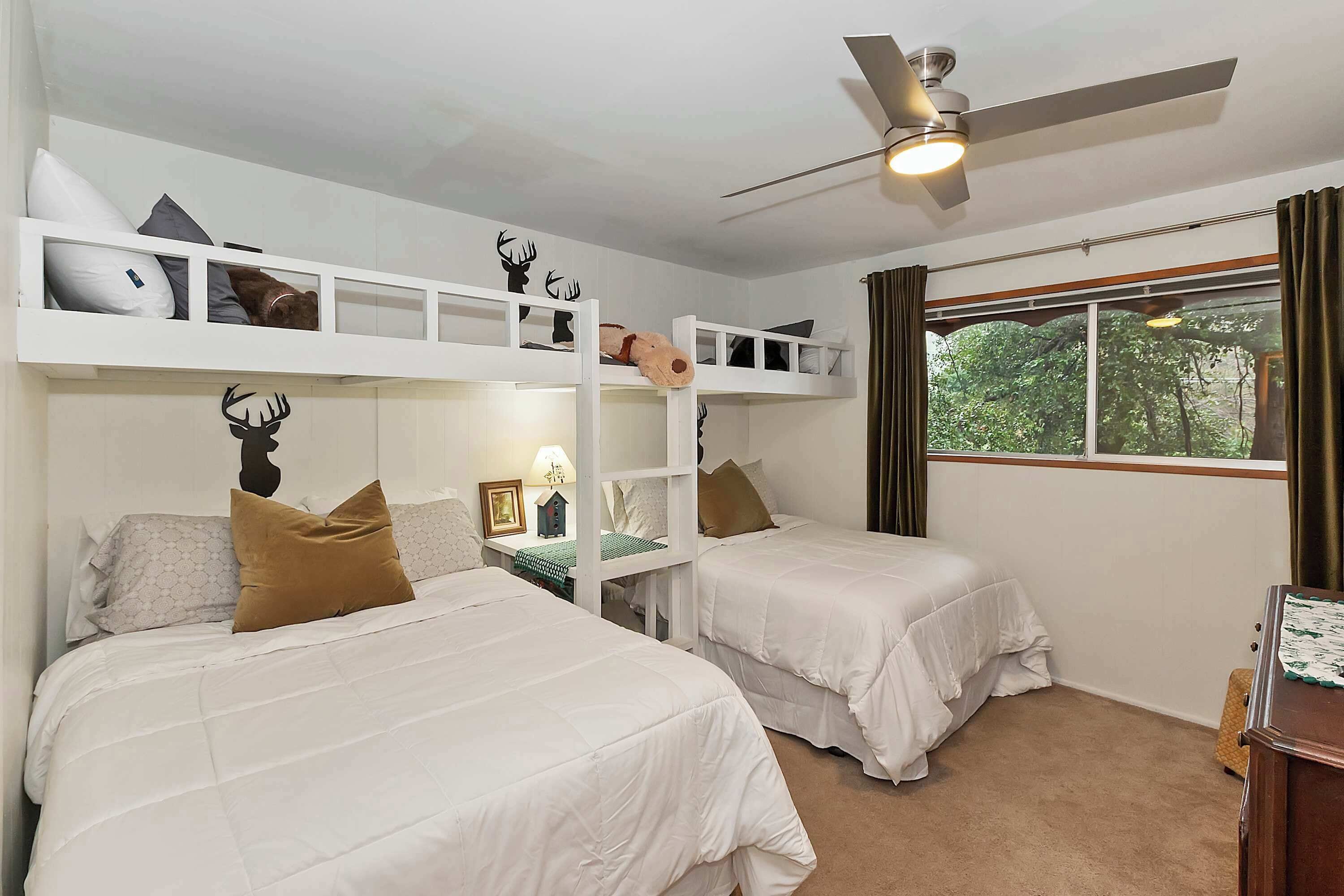 Une chambre avec deux lits superposés, un ventilateur de plafond, une fenêtre avec des rideaux et une petite table avec une lampe.