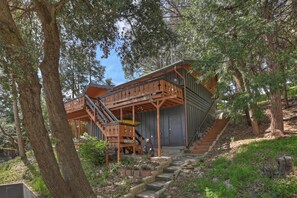 Surrounded by mature trees, this charming two-story home offers a balcony on the upper level, accessible via a stone staircase.