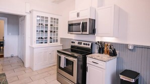 A compact kitchen with white cabinetry, a microwave, an oven, and a granite countertop.