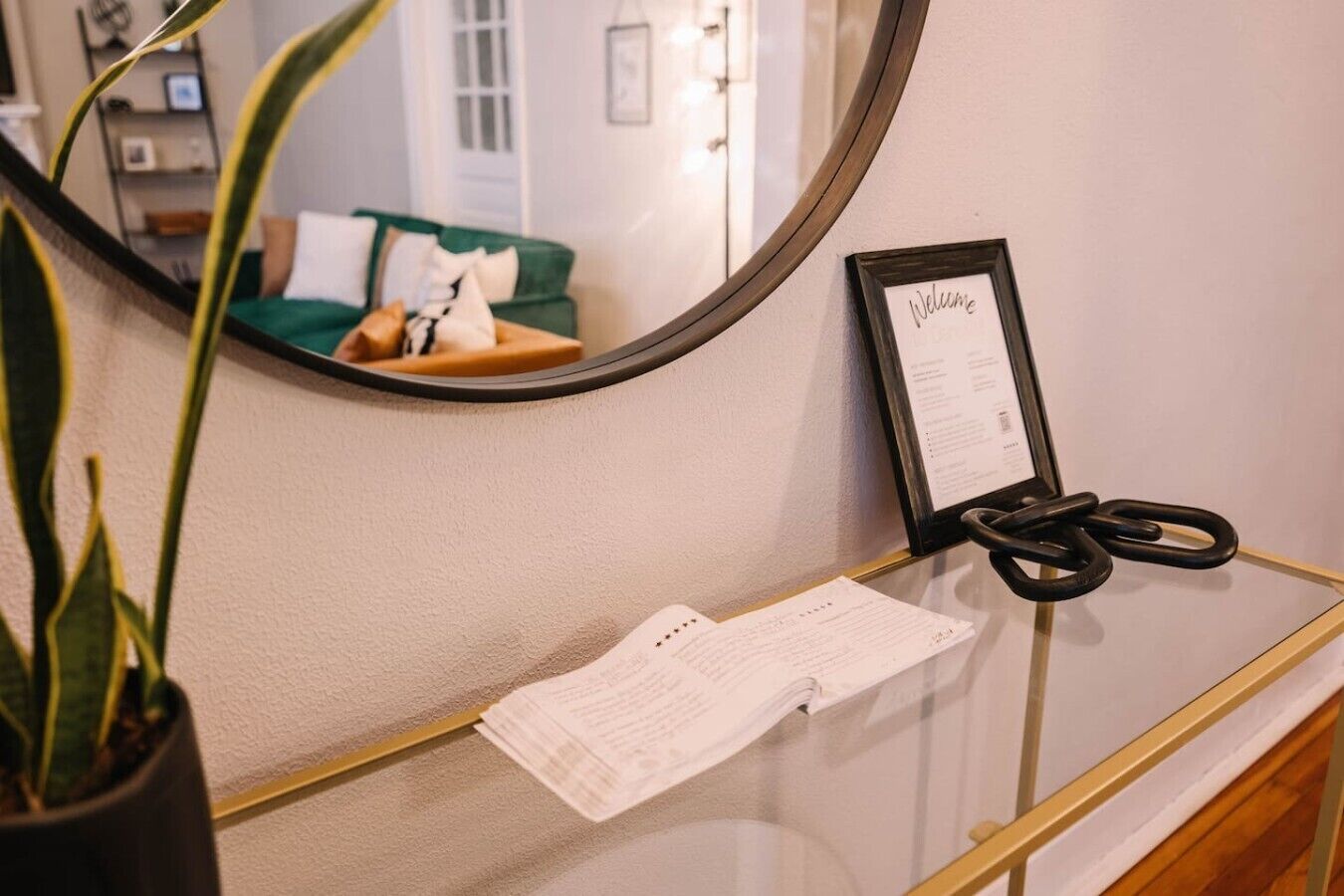 Un comptoir d’accueil avec un miroir, une pancarte de bienvenue, une paire de ciseaux et une plante.