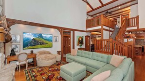 A spacious living room with a green sofa, a wooden desk, and a large painting of a mountain landscape.
