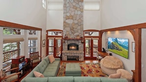 A spacious living room with a stone fireplace, comfortable seating, and large windows.