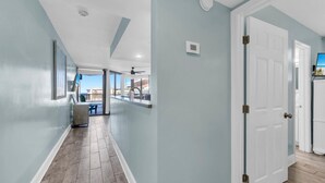 A hallway with a view to a balcony, a door, and a thermostat on the wall.
