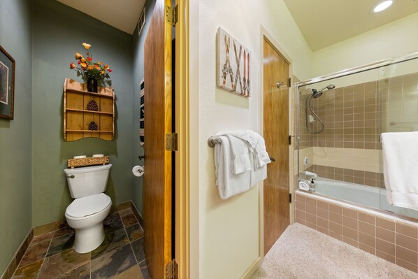 A bathroom with a toilet, shower, and a wooden shelf with decorative items.