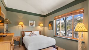 Una camera da letto ordinata con un letto, lampade da comodino, un comodino in legno e una finestra con vista su alberi e montagne.