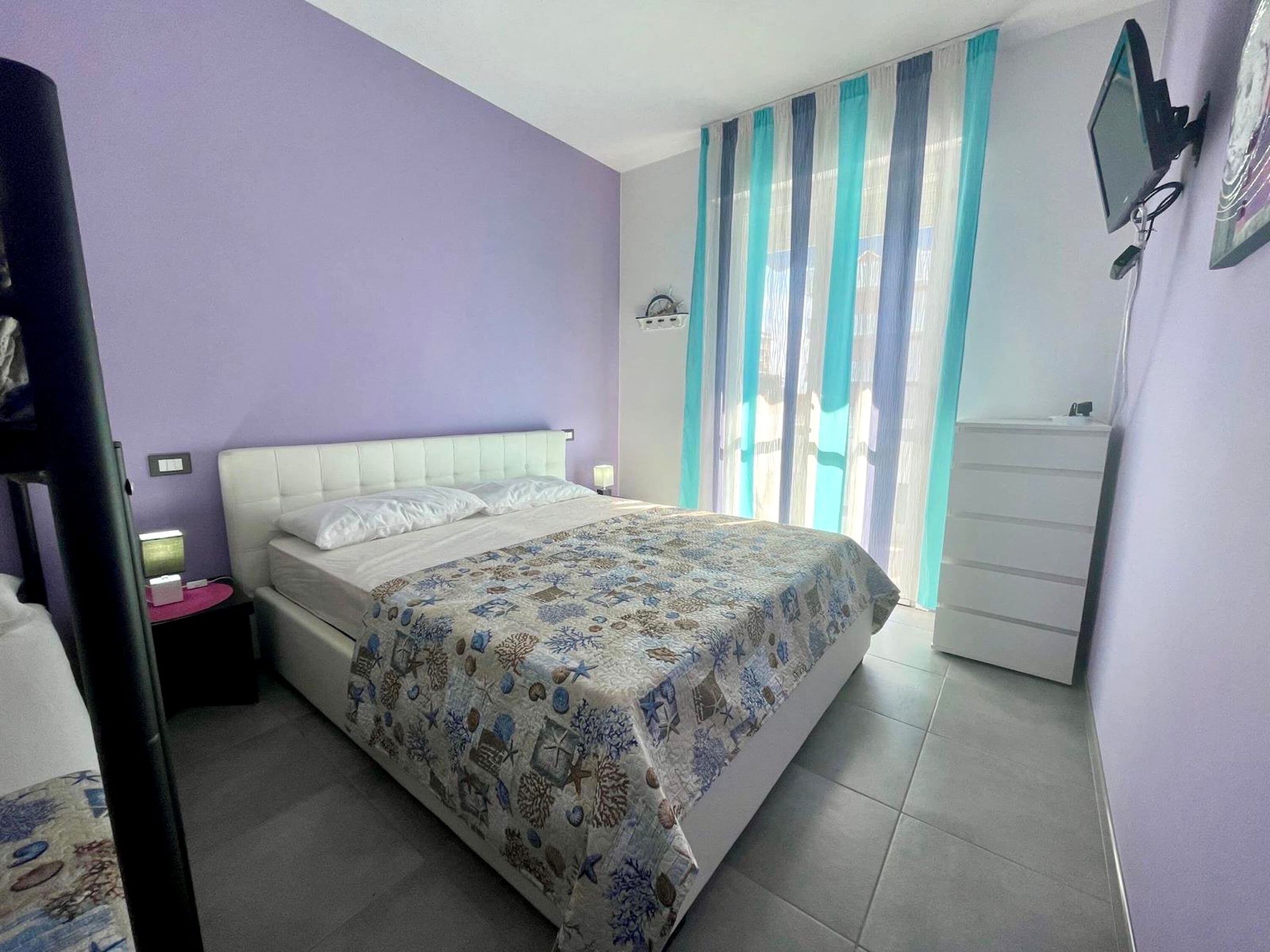 A bedroom with a bed, a nightstand, a dresser, and a TV mounted on the wall.