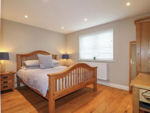 Une chambre à coucher avec un lit en bois, des lampes de chevet, une fenêtre avec des stores et un radiateur.
