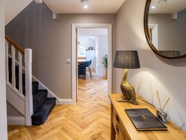 Un pasillo con suelo de madera, una escalera con barandillas blancas, un escritorio con lámpara y un espejo en la pared.