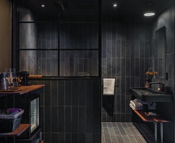 A modern bathroom with dark tiles, a wooden vanity, a sink, and a shower area. - Maison Grinder (Montréal)