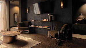 A modern living room with a flat-screen TV mounted on the wall, two armchairs, a coffee table, and a bookshelf with books and decorative items. - Maison Grinder (Montréal)