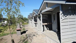 A row of wooden cabins with balconies, a paved pathway, and a small tree. - Holiday Home in Dziwnówek near Baltic Sea (Dziwnówek)