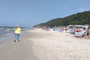 Une plage où l’on voit des gens se promener et s’asseoir sur le sable, ainsi que des parasols et des chaises de plage.
