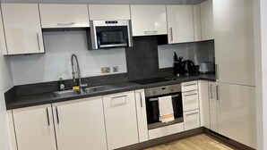A modern kitchen with white cabinets, a stainless steel sink, a microwave, and a built-in oven. - 1-Bed Apt, Sleeps 4, Near Attractions & Transport (Lewisham)
