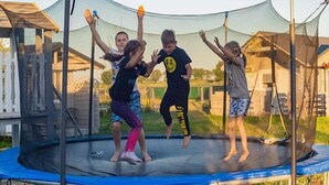 A trampoline with a safety net, surrounded by a wooden fence and a house in the background. - Holiday Home Dziwnówek near Baltic Sea (Dziwnówek)