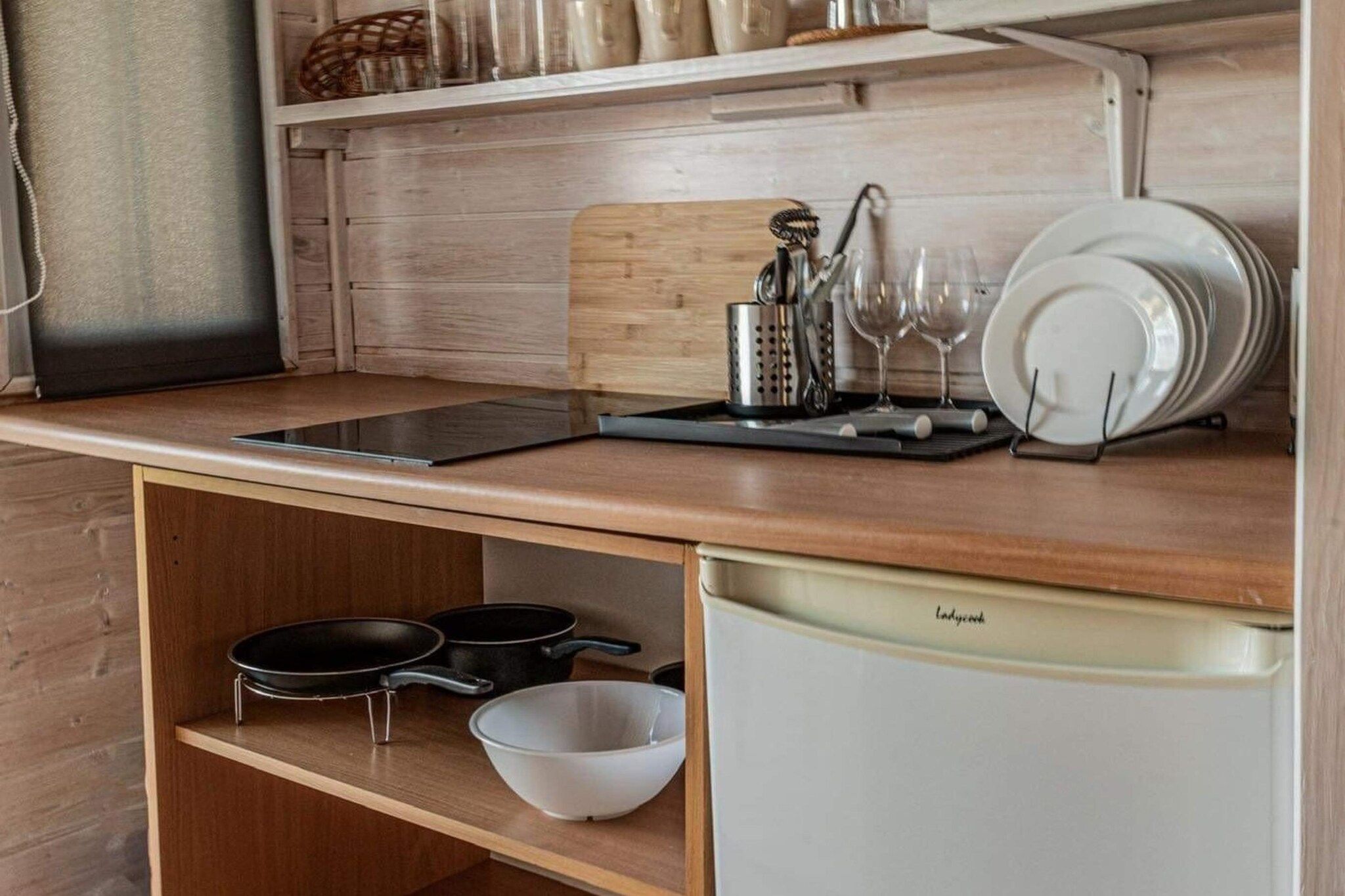 A compact kitchen with a wooden countertop, a built-in dishwasher, and a shelf with cookware.