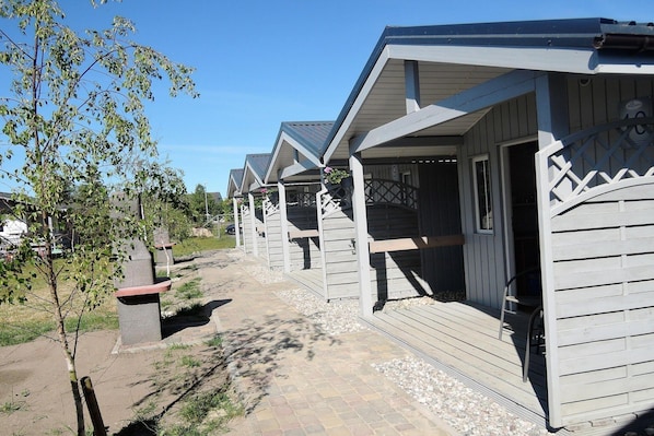 A row of wooden cabins with a paved walkway, a small tree, and a bench.