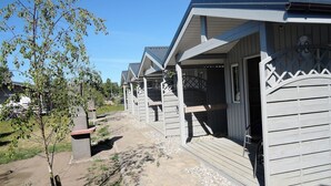 A row of wooden cabins with balconies, a paved pathway, and a small tree. - Holiday Home Dziwnówek near Baltic Sea (Dziwnówek)